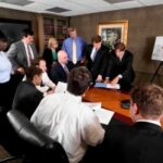 Diverse corporate team discusses strategies using documents and digital tools in a formal boardroom.