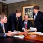 Four professionals discuss documents in a well-equipped corporate office setting.