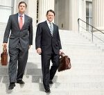 Mark and Ken, in suits, descend steps at a government building, briefcases in hand.