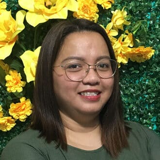 Person smiling in green, framed by lush leaves and vibrant yellow flowers.