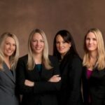 Four professional women in business attire exude unity and confidence in a corporate setting.