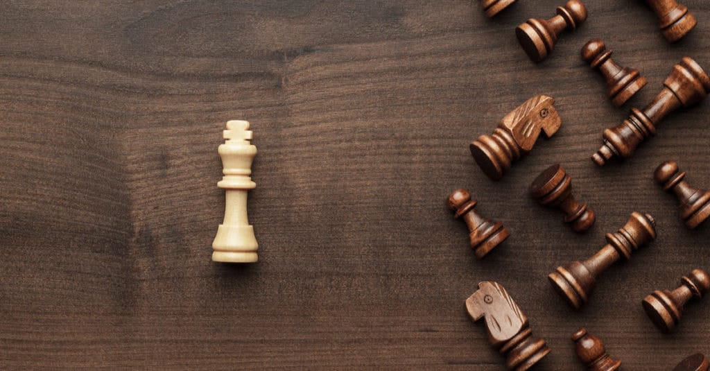 White king stands victorious among fallen dark chess pieces on a textured board.