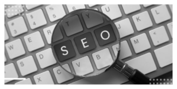 Close-up of SEO keys under magnifying glass on black-and-white keyboard.