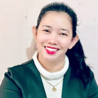 Smiling asian woman in a green blazer, with subtle makeup, posing for a professional portrait.
