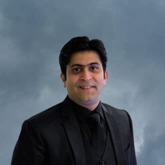 Nikhil sethis portrait: friendly smile, dark suit, soft-lit against a cloudy backdrop.