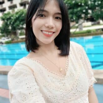 Young woman in pale yellow top takes a cheerful selfie at a sunny poolside resort.