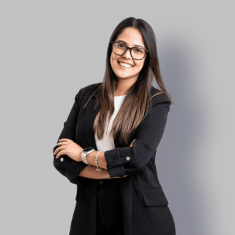 Confident businesswoman in black blazer smiles against a gradient gray background.