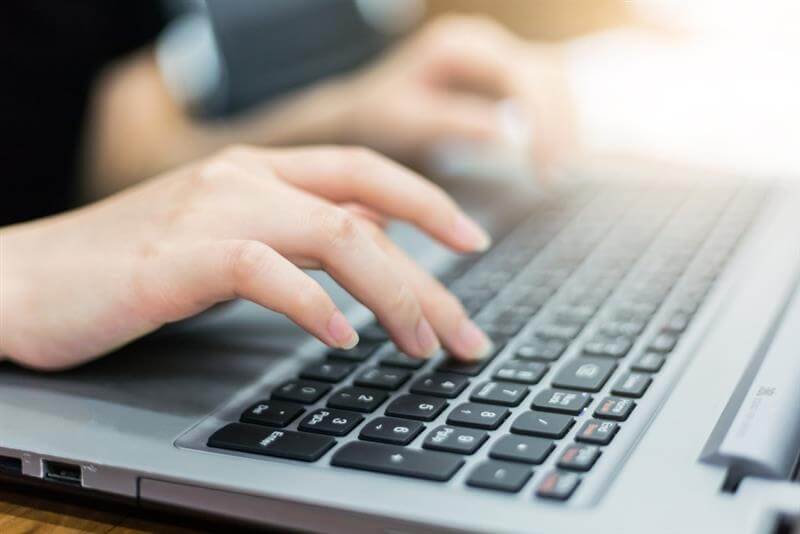 A close-up hand image of a woman working on her laptop computer, typing on the laptop keyboard, responding to emails.